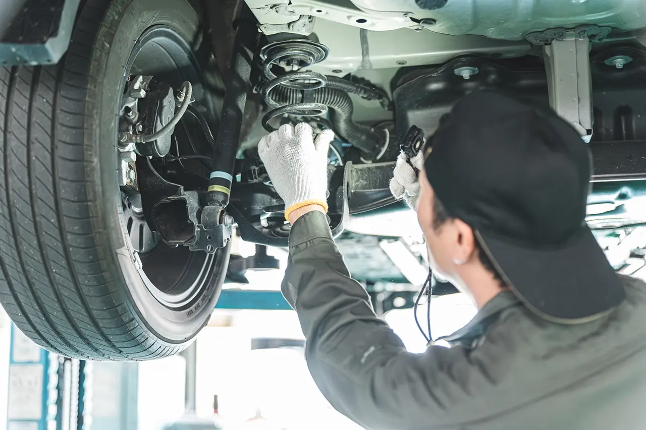リフト下の車でサスペンションを点検する整備士