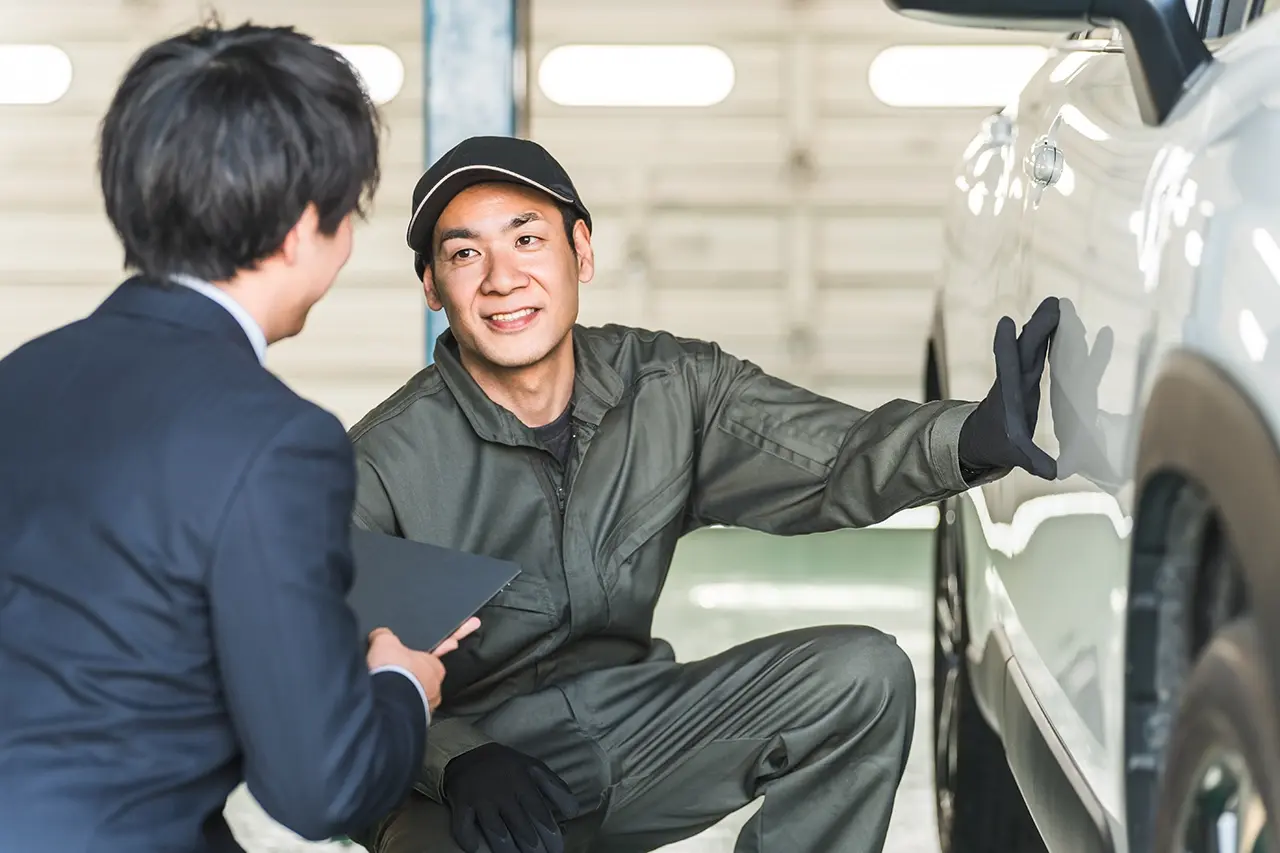 車のボディ状態を確認し合う整備士と男性